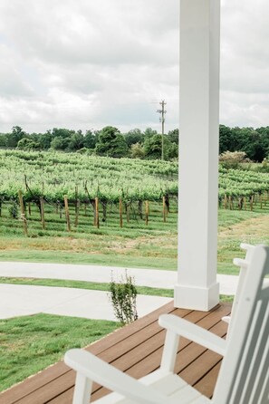 Ein überdachter Außenbereich mit Holzterrasse, weißen Stühlen und einem Weinberg im Hintergrund.