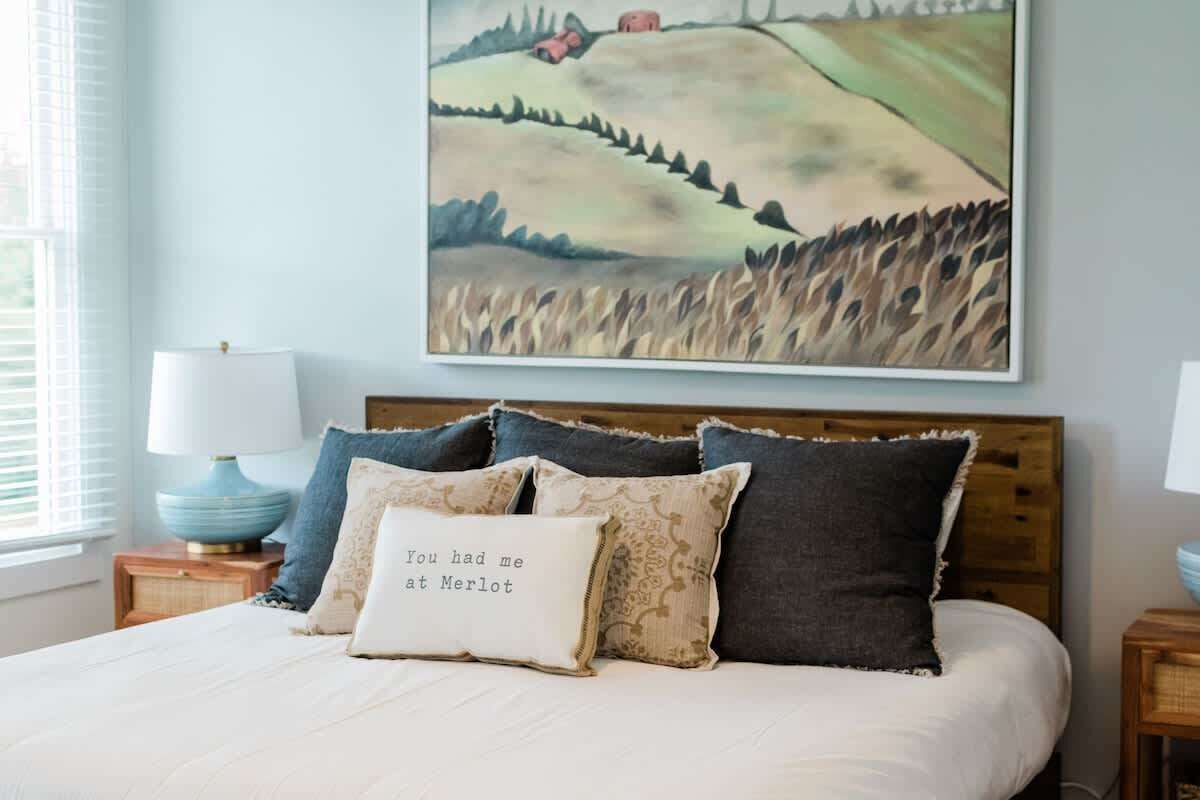 A bedroom with a bed, pillows, a nightstand, a lamp, and a painting on the wall.
