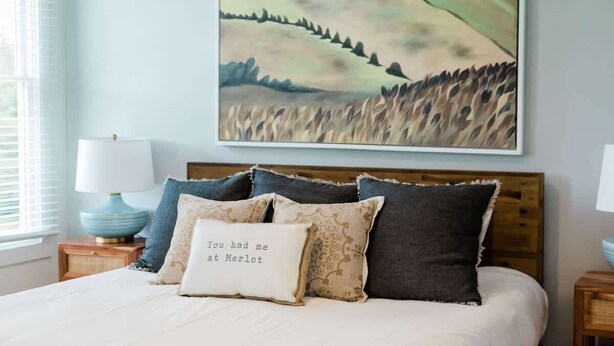 Ein Schlafzimmer mit einem Bett, Kissen, einem Nachttisch, einer Lampe und einem Bild an der Wand.