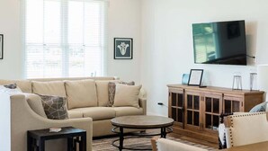 Ein Wohnzimmer mit einer Couch, einem Couchtisch, einem Schrank und einem an der Wand befestigten Fernseher.