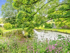 A serene garden with a pond, lush greenery, and flowering plants. - 5 bedroom accommodation in Slapton (Slapton)