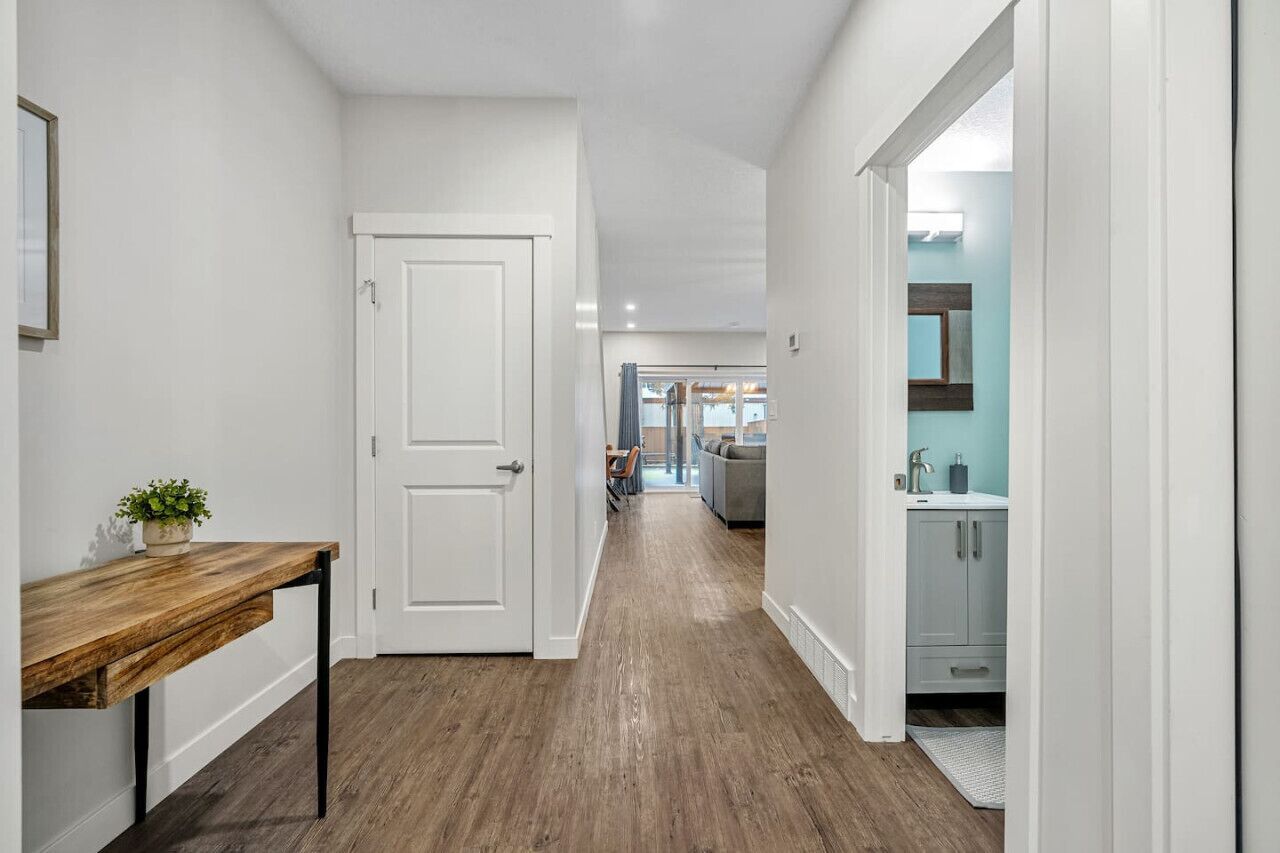 A hallway with a wooden bench, a white door, and a view into a living area with a sofa and a dining table.