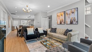 A modern living room with a sofa, armchairs, and a coffee table. There is a dining area with a table and chairs. The room has a chandelier and artwork on the wall. - 6BD/5BTH + Roofdeck - Downtown Chicago! (Chicago)