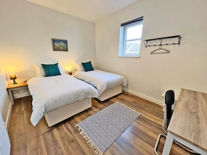A bedroom with two beds, a window, a hanging clothes rack, and a patterned rug.