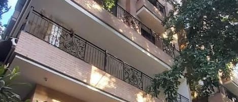 A multi-story building with balconies, arched doorways, and surrounding greenery.