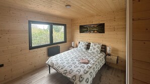 Un dormitorio con techo de madera, un ventanal grande, una cama con ropa de cama estampada y un cuadro en la pared.