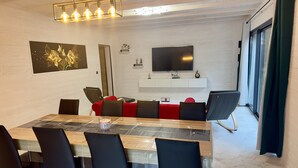 Un comedor moderno con una mesa de madera, sillas tapizadas en negro y rojo, una vela de cristal y un televisor de pantalla plana montado en la pared.