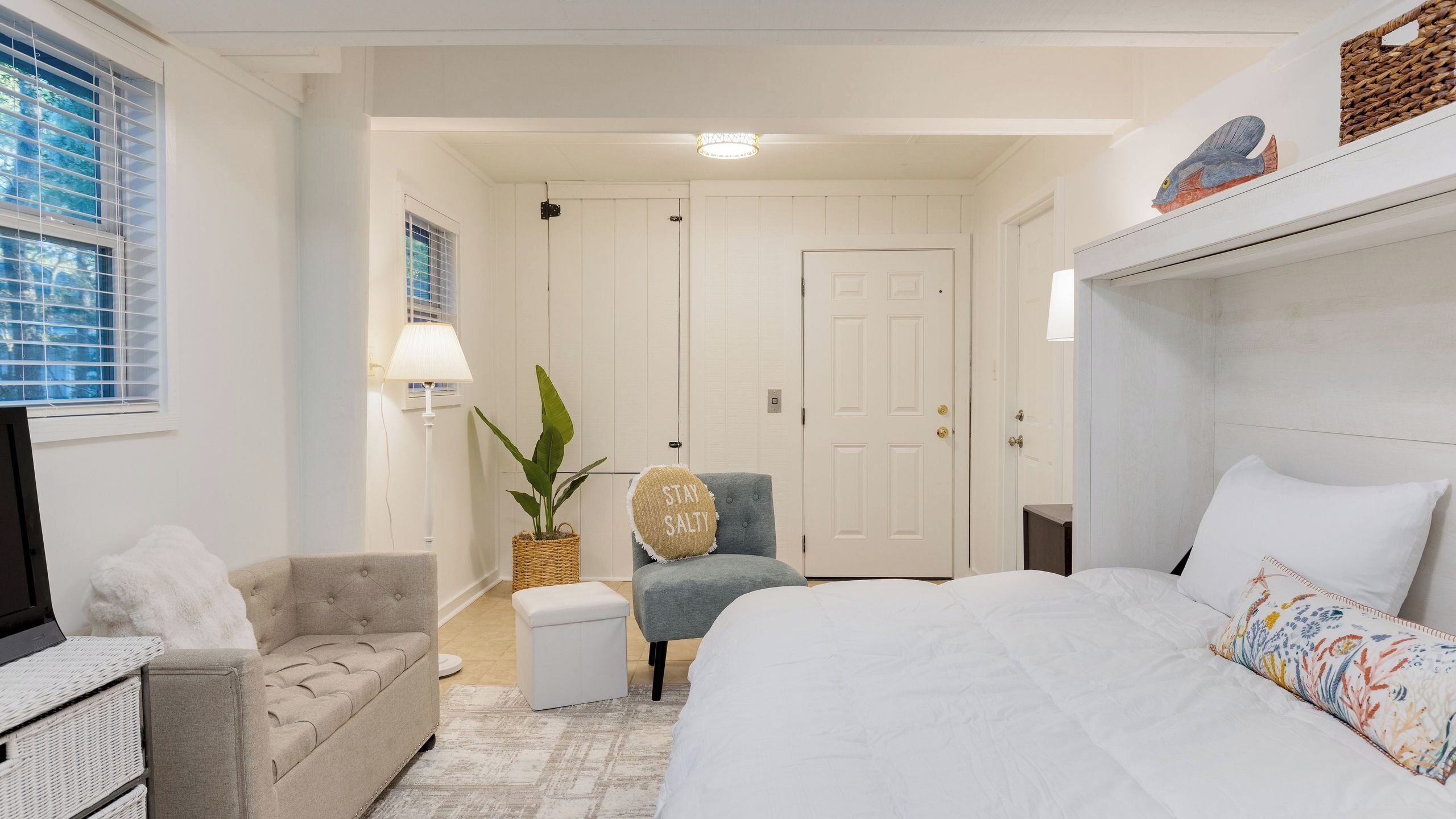 A hotel room with a bed, a chair, a sofa, a lamp, a plant, and a television.