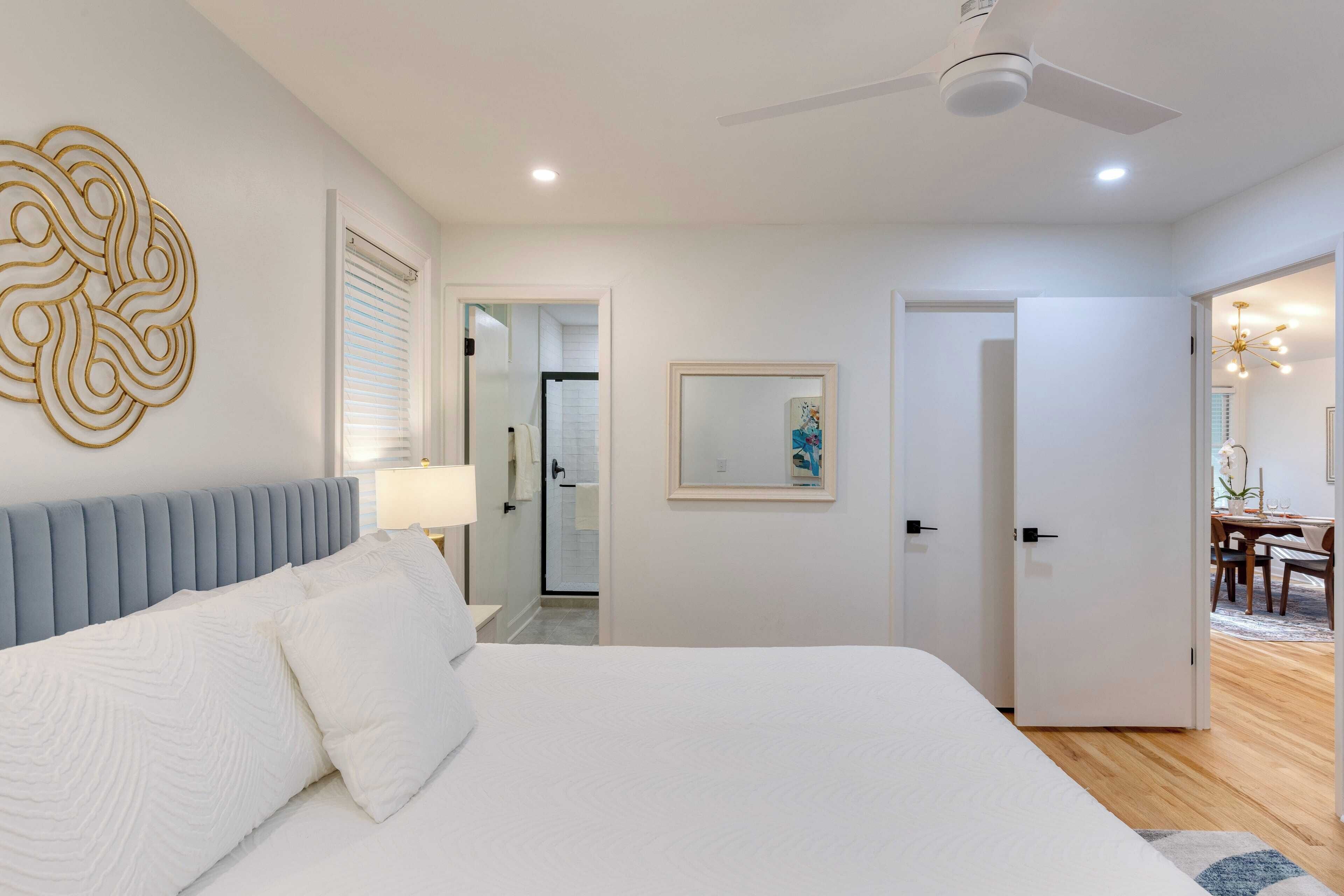 A modern bedroom with a large bed, a ceiling fan, and a bathroom visible through an open door.