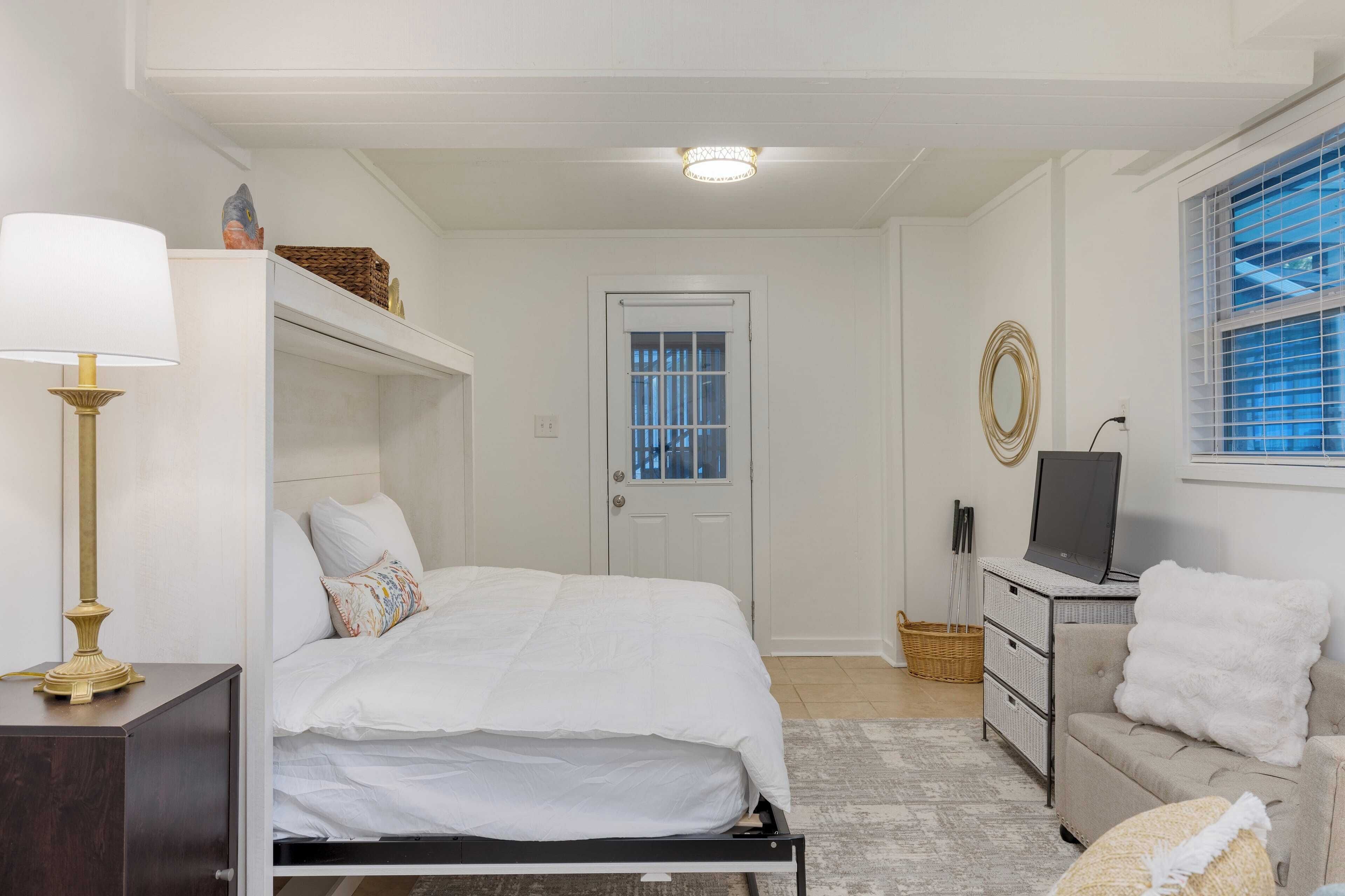 A bedroom with a bed, a desk with a computer, a chair, a lamp, and a window with blinds.