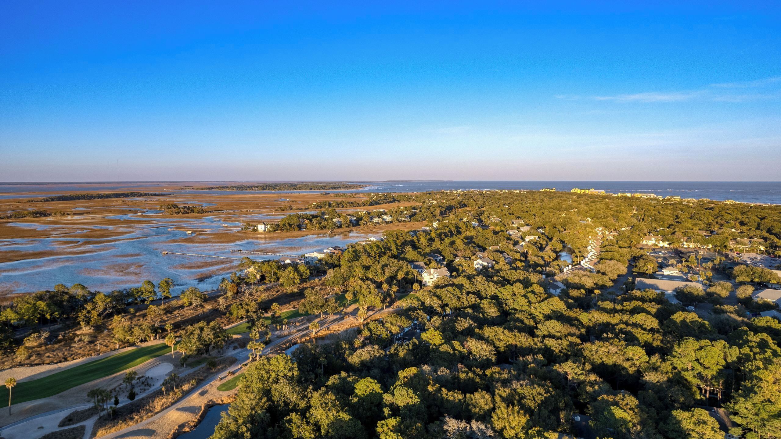 An aerial view of a coastal area with residential buildings, a golf course, and a large body of water.