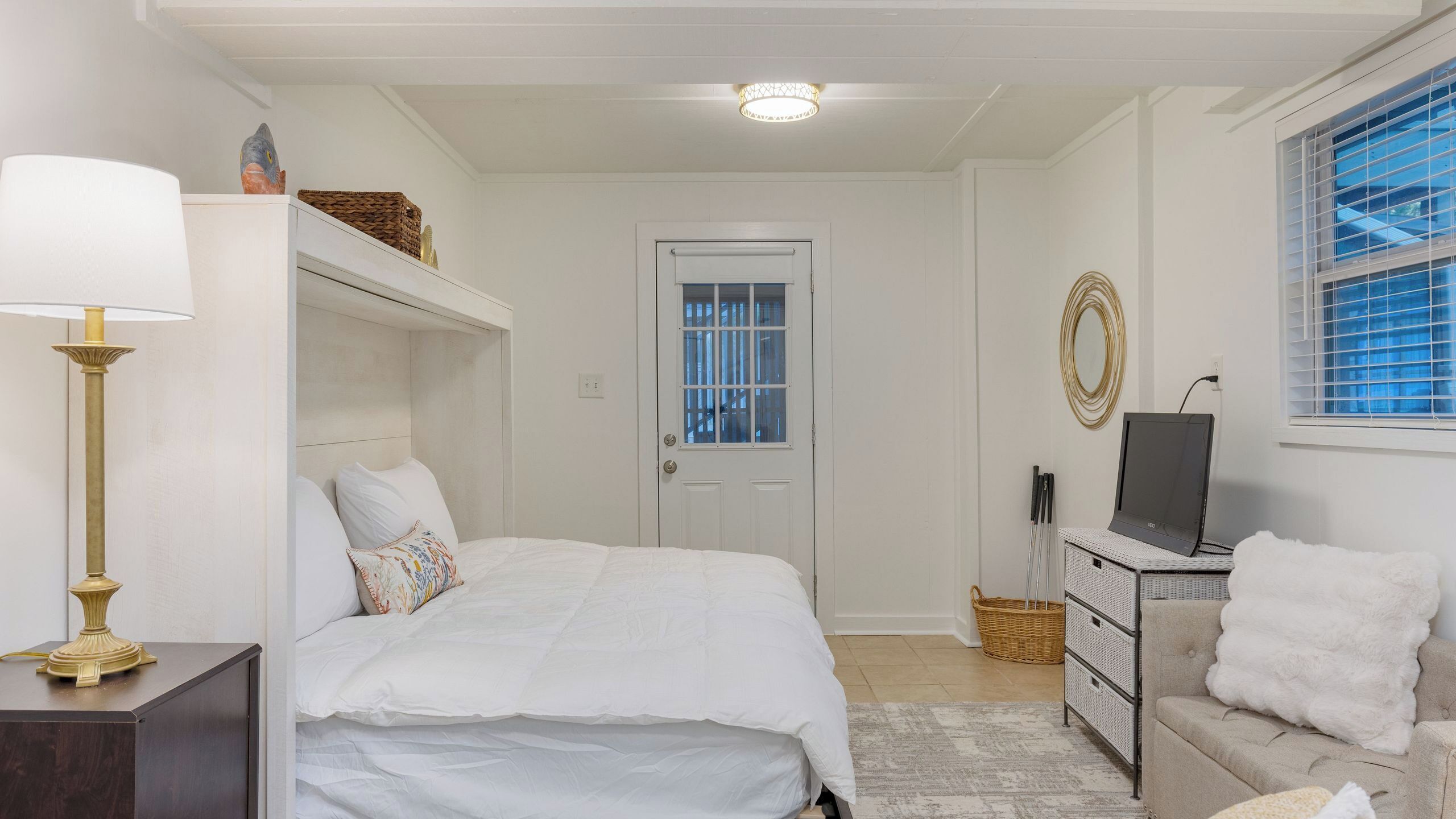 A bedroom with a bed, a dresser, a television, a lamp, and a window with blinds.