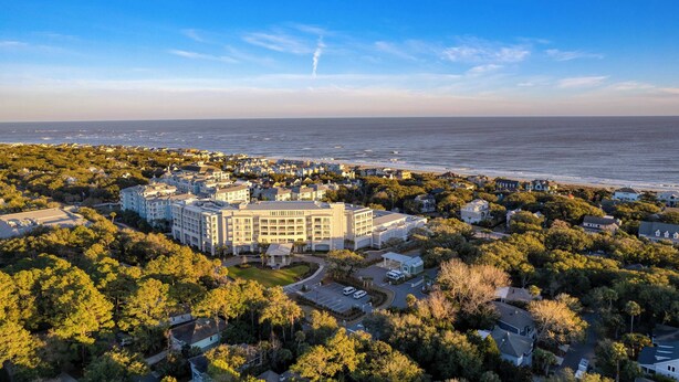 A coastal hotel with multiple buildings, surrounded by dense greenery and a view of the ocean. - Conch Cottage by Avantstay Walk to Beach, Deck, Fireplace, Outdoor Dining (Isle of Palms)
