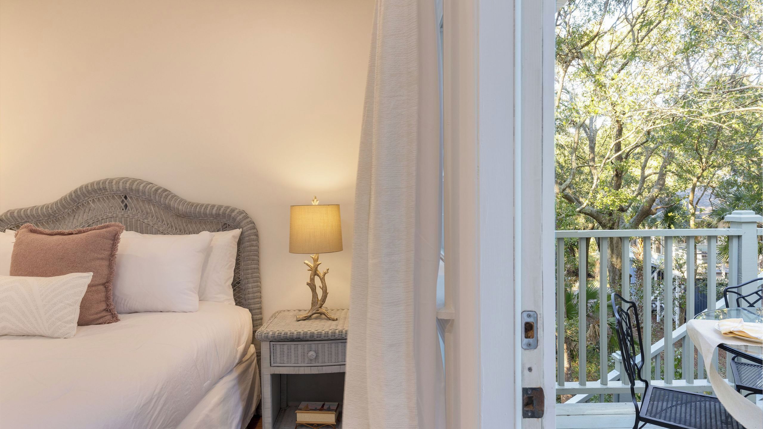 A bedroom with a bed, bedside table, lamp, and a view of the outdoor balcony.