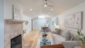 A spacious living area with a fireplace, a sofa, a coffee table, and a dining area in the background. - Conch Cottage by Avantstay Walk to Beach, Deck, Fireplace, Outdoor Dining (Isle of Palms)