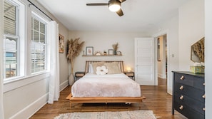 A bedroom with a bed, a ceiling fan, a dresser, and a window.