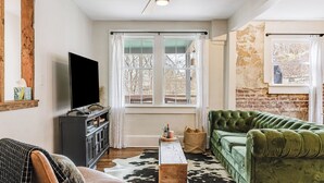 A living room with a television, a green sofa, a wooden coffee table, and a window with curtains. - Riverside Trade Retreat Avantstay Industrial-chic, Near Downtown Asheville (Asheville)