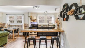 A modern kitchen with a central island, black bar stools, and a dining area with a green sofa. - Riverside Trade Retreat Avantstay Industrial-chic, Near Downtown Asheville (Asheville)