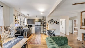A spacious kitchen with a central island, a dining area with a green sofa, and a living room with a wooden floor.