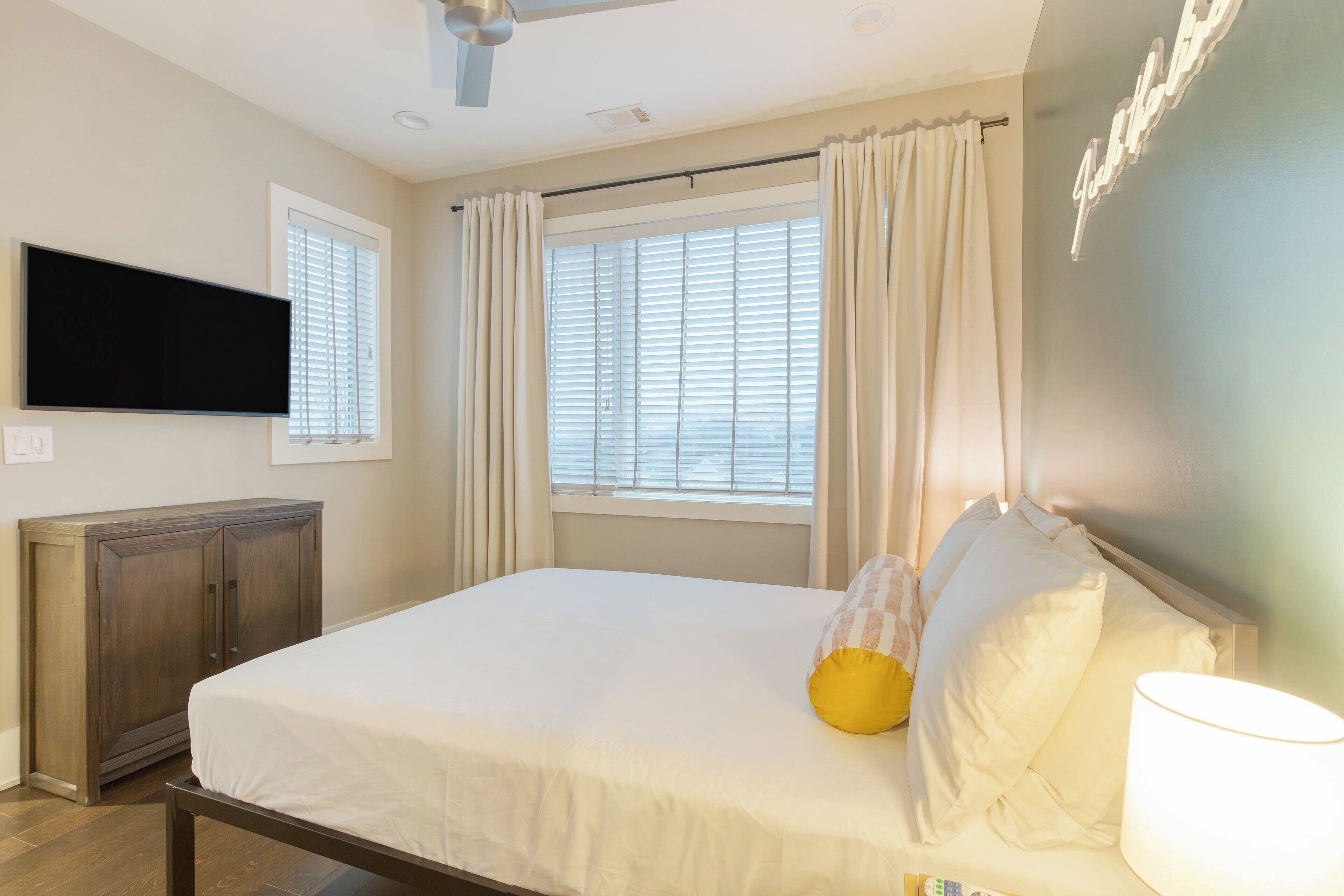Un dormitorio con cama, cortinas, un televisor de pantalla plana y un ventilador de techo.