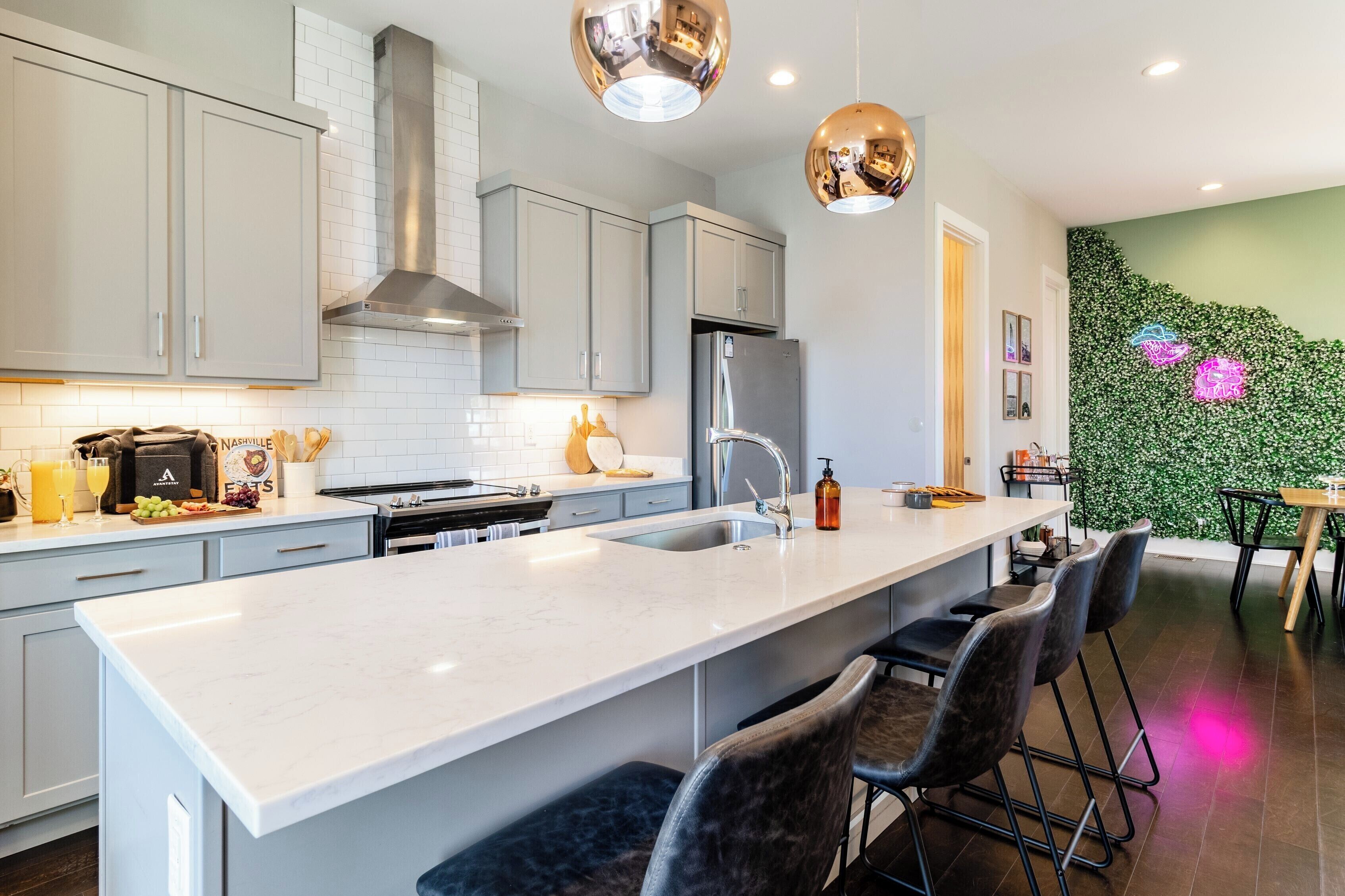 A modern kitchen with a central island, bar stools, and a green wall with floral patterns.