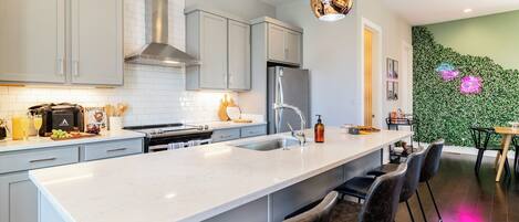 A modern kitchen with a central island, bar stools, and a green wall with floral patterns.