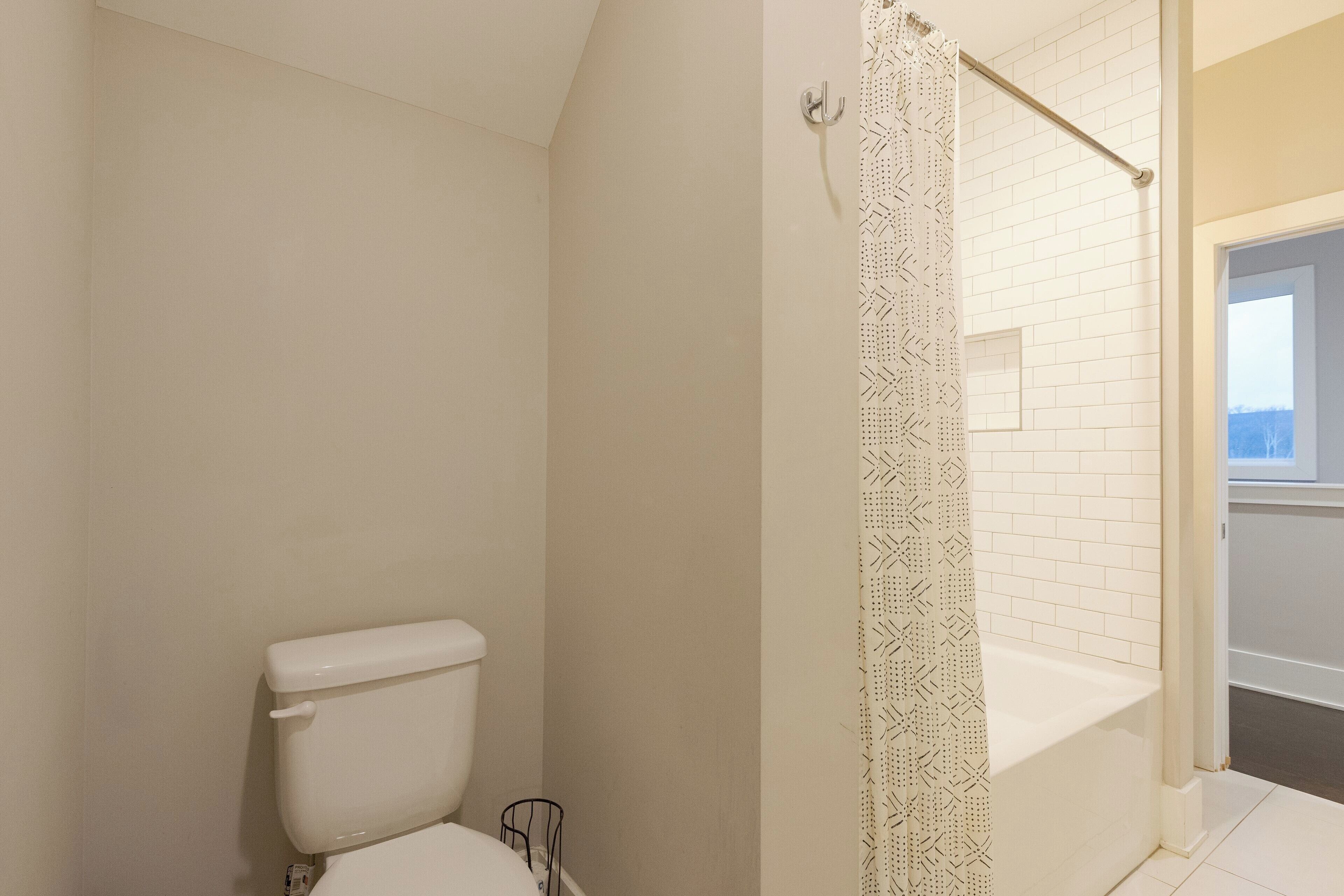 Uma casa de banho com sanita, chuveiro com cortina estampada e parede revestida a azulejos brancos.