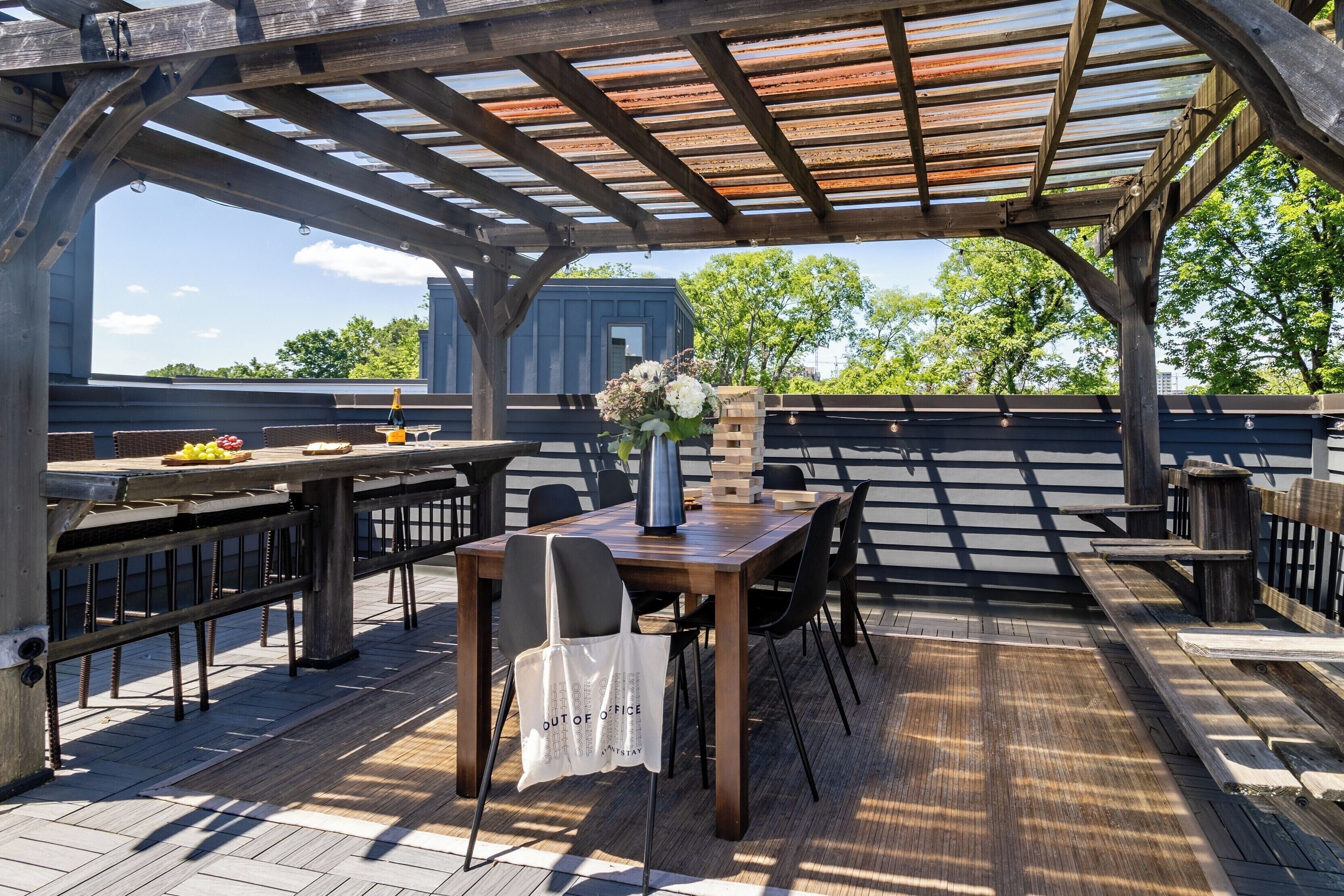 An outdoor patio with a wooden table, chairs, a white tote bag, and a vase with flowers.