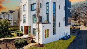 A modern two-story house with a white exterior, large windows, and a small front yard with a tree and shrubs. - Huge Private Rooftop Deck w/ Firepit + Putt-putt 8 Mins to Broadway Doralee (Nashville)