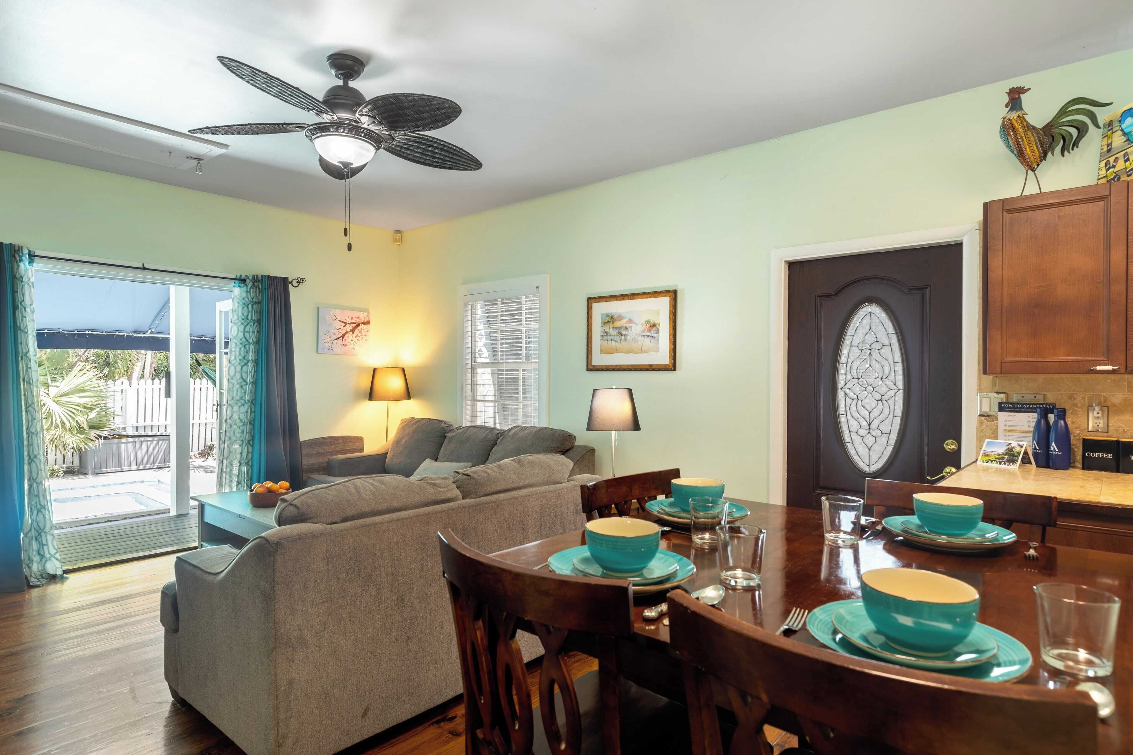 Un coin repas avec une table dressée pour quatre personnes, un ventilateur de plafond et une vue sur l’extérieur.