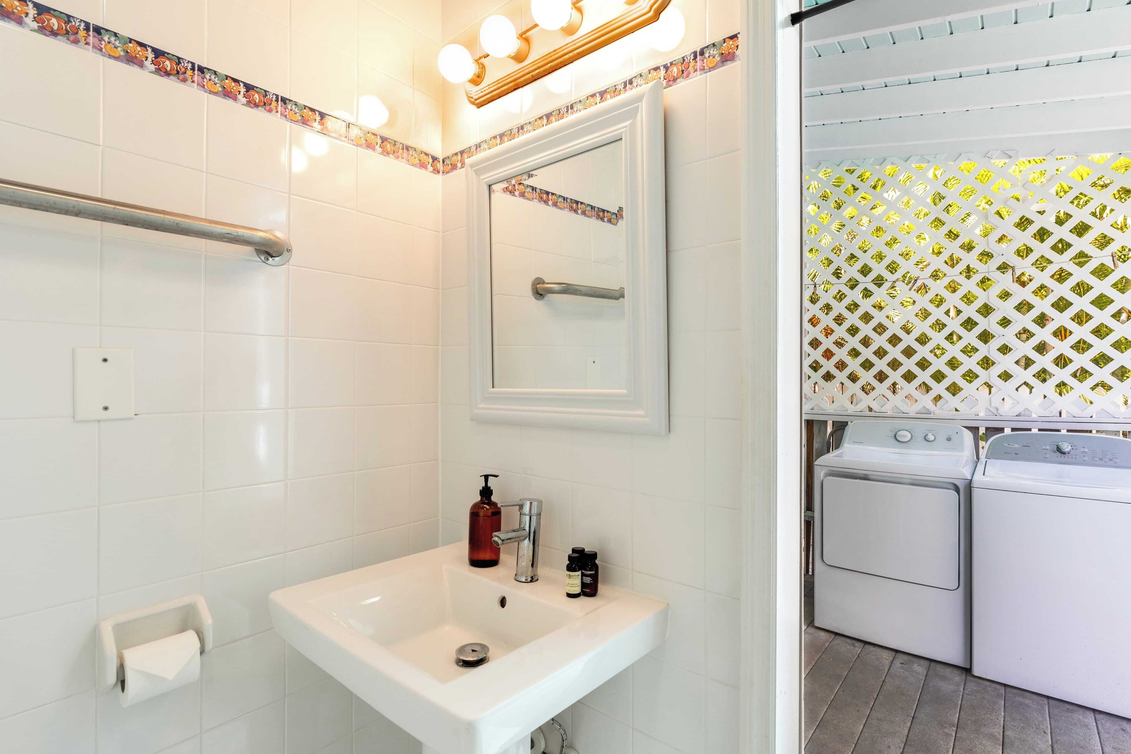 Une salle de bain équipée d’un lavabo, d’un miroir, d’un distributeur de serviettes et d’un espace buanderie avec des machines à laver.