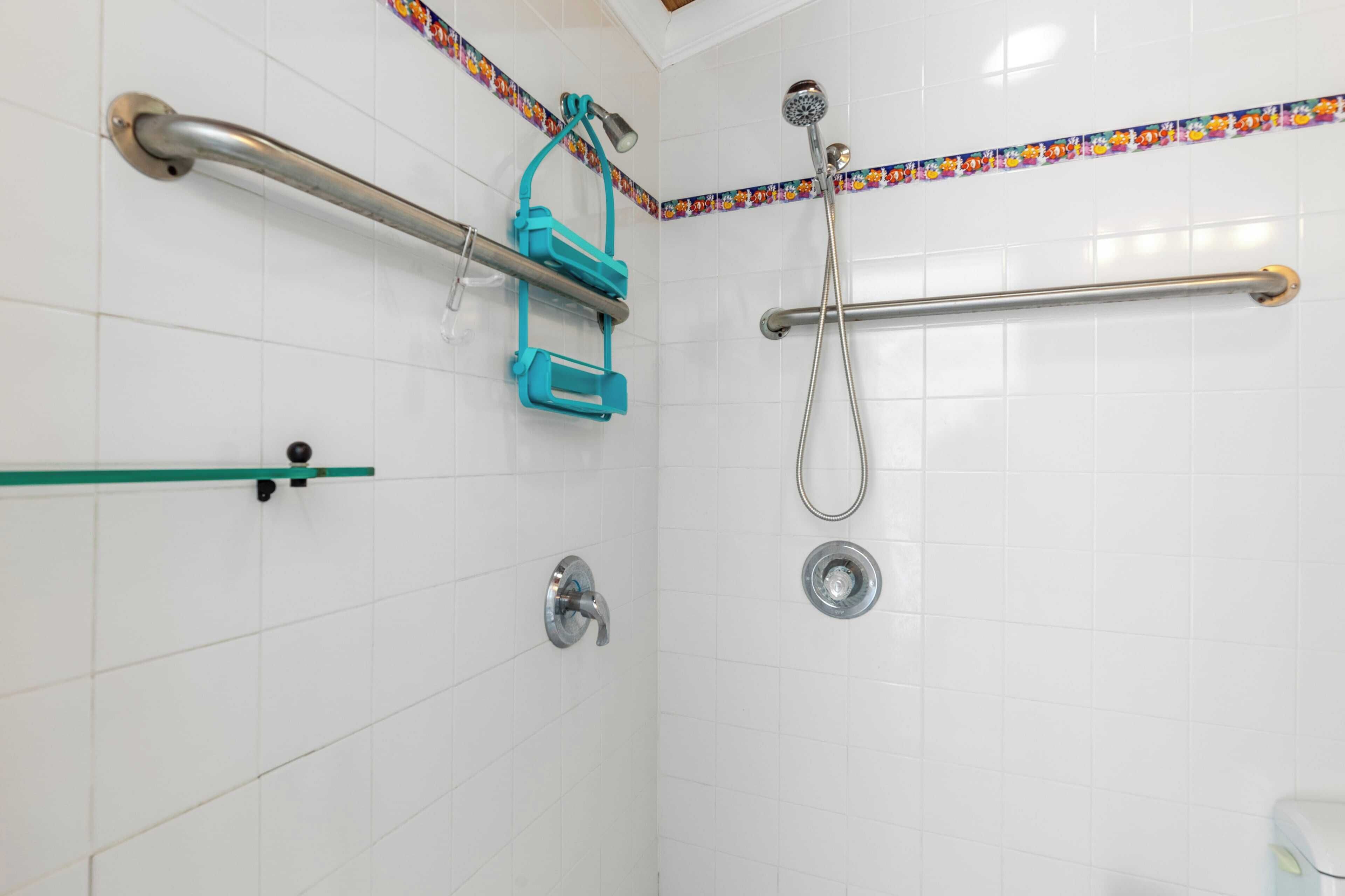 A bathroom with white tiled walls, a shower with a handheld showerhead, a grab bar, and a green safety bar.