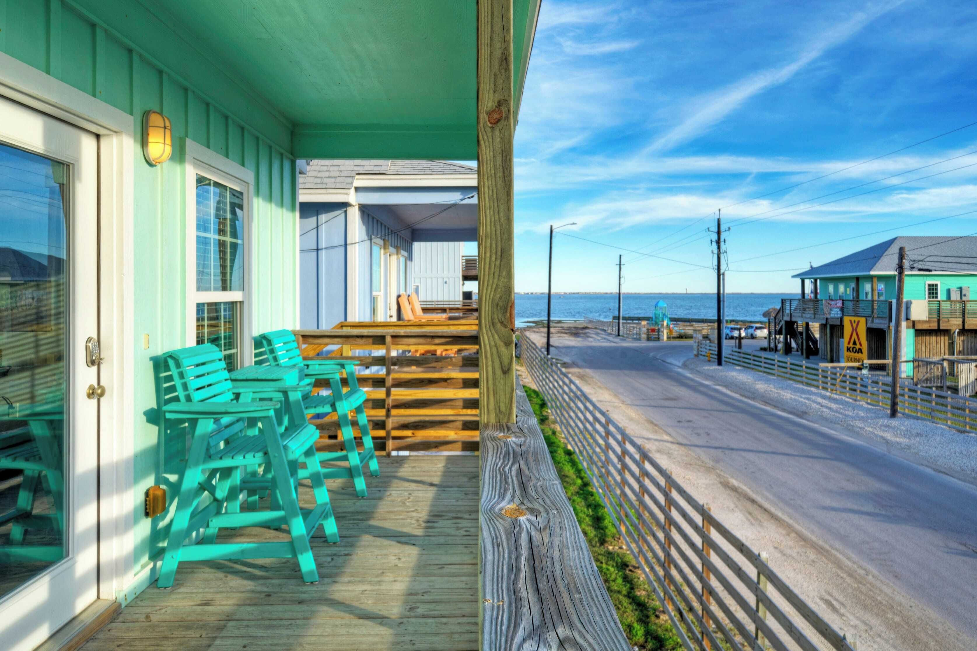 A wooden deck with chairs, a wooden fence, and a view of the beach and ocean.