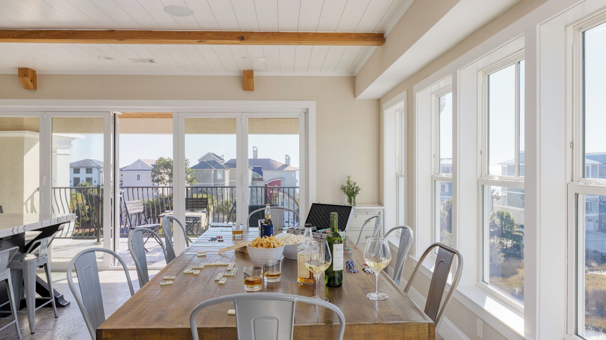 A dining area with a wooden table, chairs, a bowl of chips, wine glasses, and bottles.