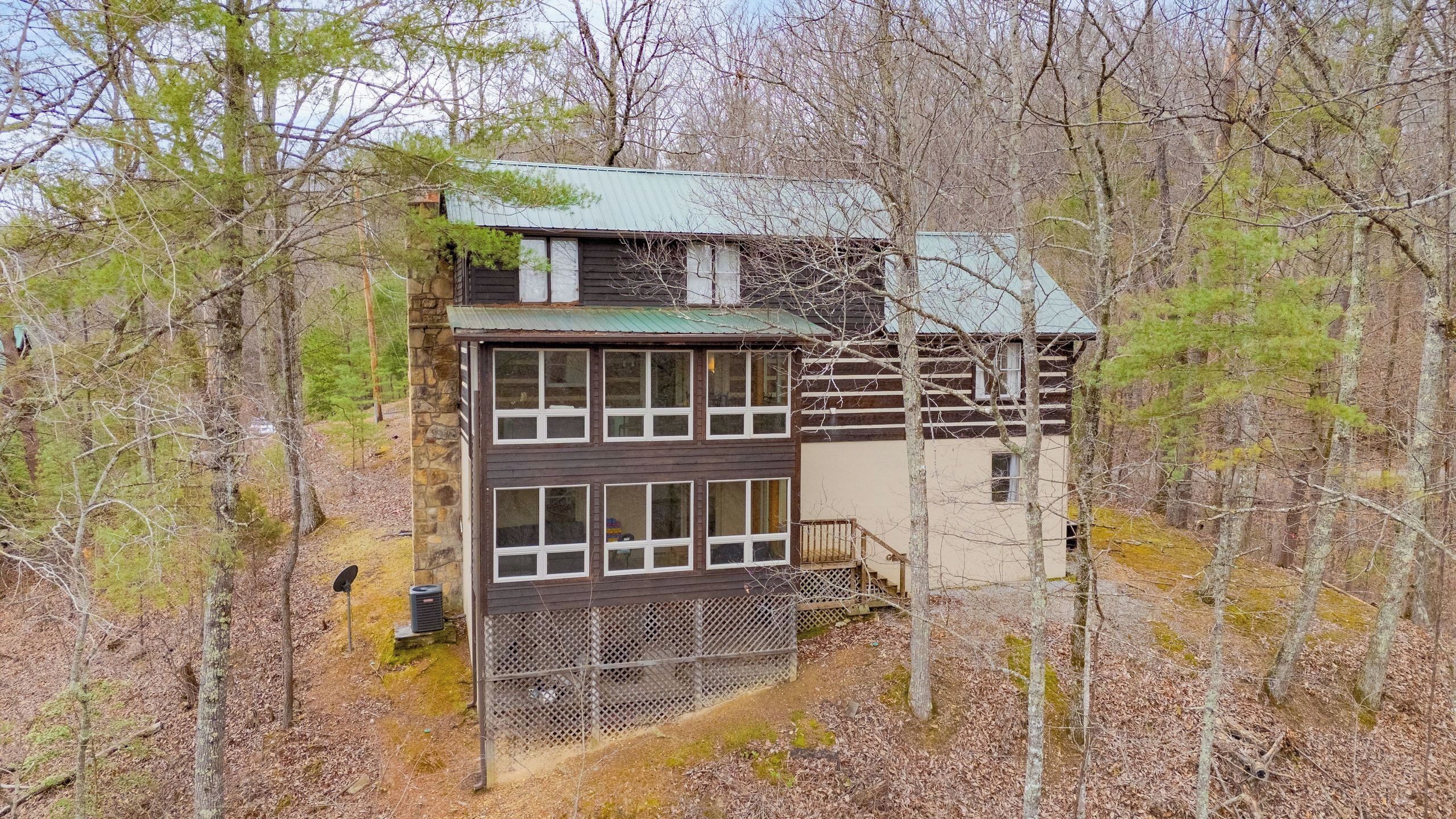 A cabin with a stone foundation, multiple windows, and a metal fence.