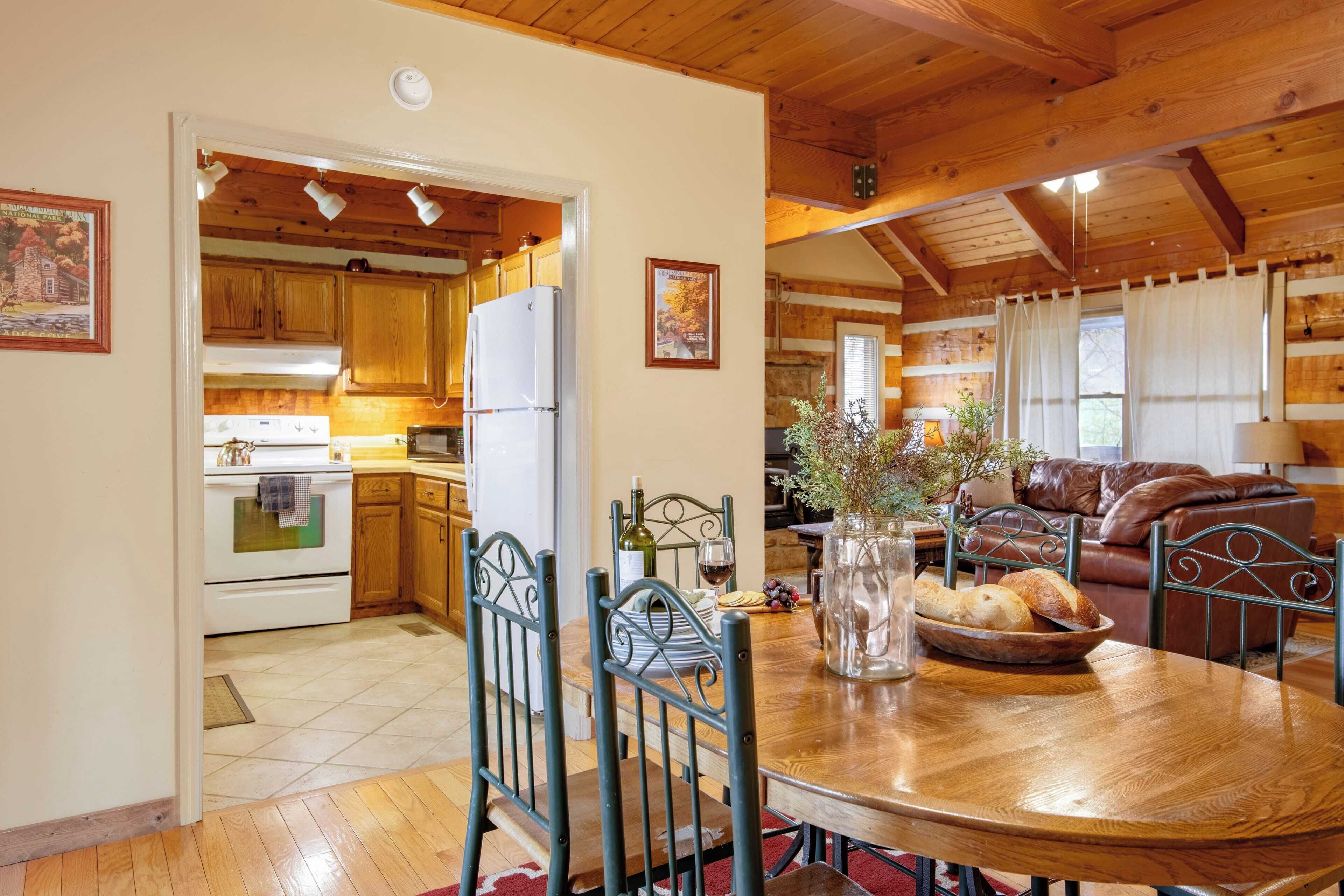A wooden interior with a dining table, chairs, a kitchen area with wooden cabinets and appliances, and a living area with a couch and a lamp.