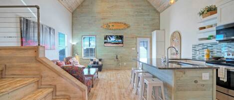A spacious kitchen with wooden flooring, a central island, and a view of the beach through a window.