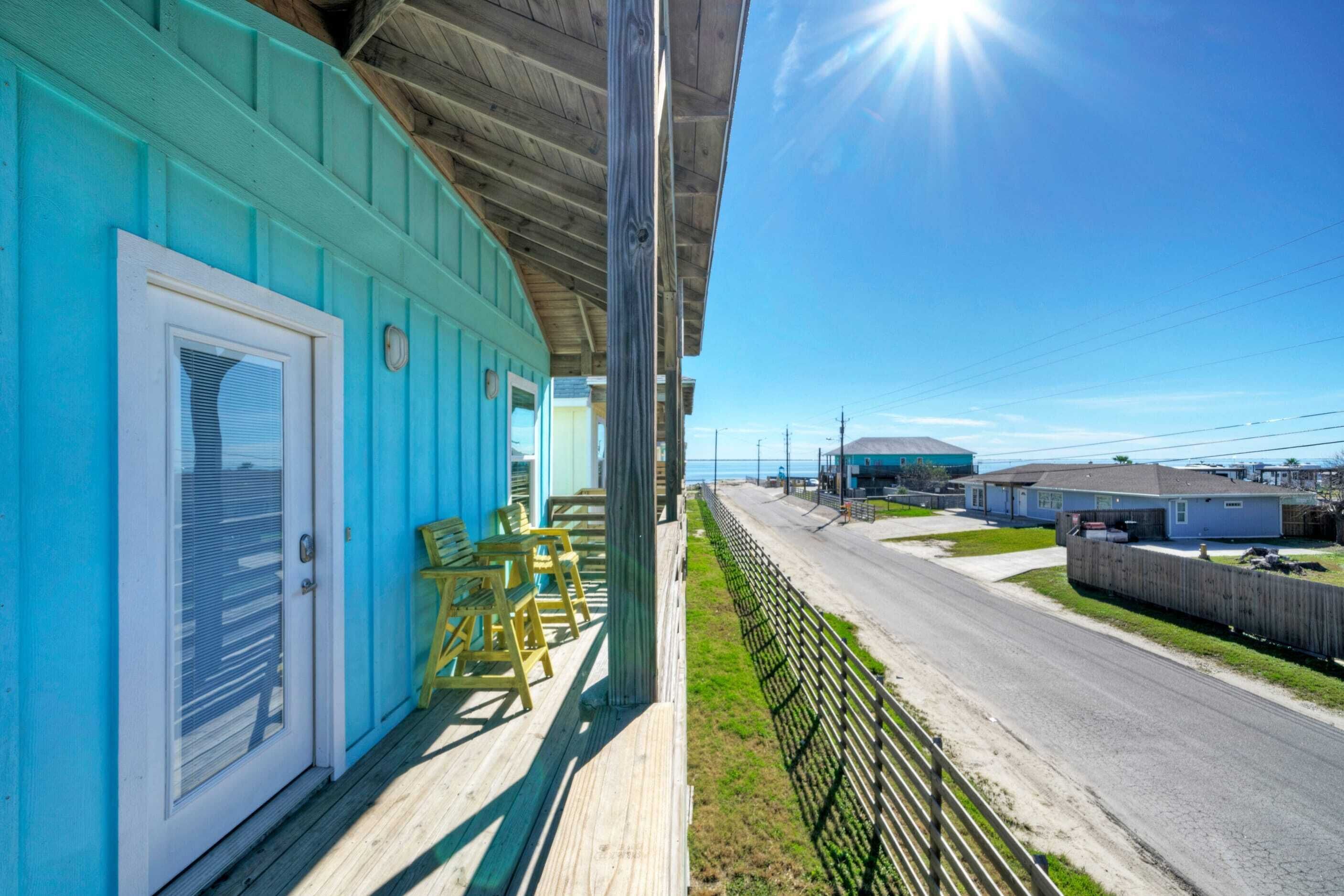 A coastal building with a wooden deck, a covered porch, and a view of the beach and ocean.