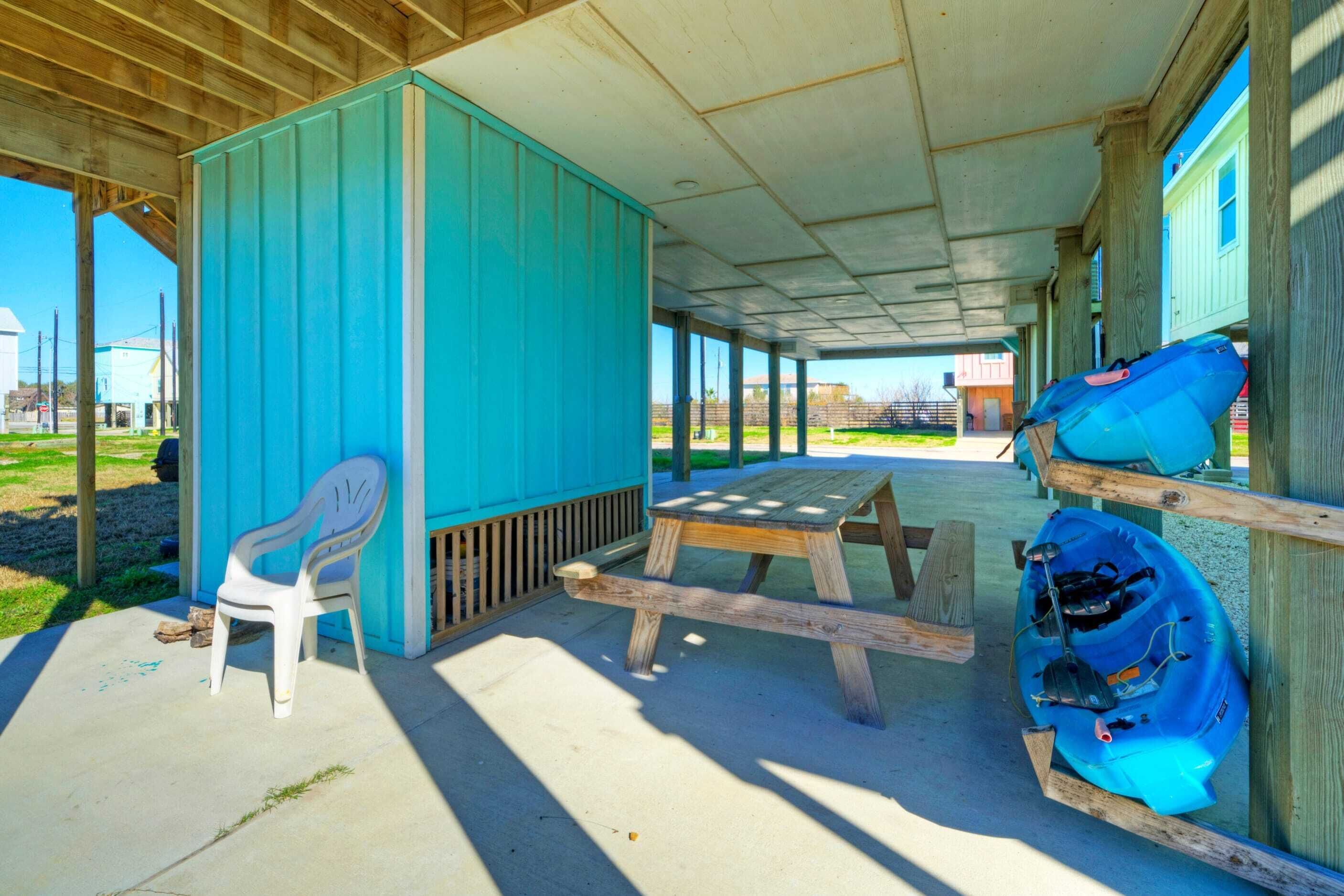 Un espace extérieur abrité comprenant une table de pique-nique, une chaise en plastique blanche et un kayak bleu.