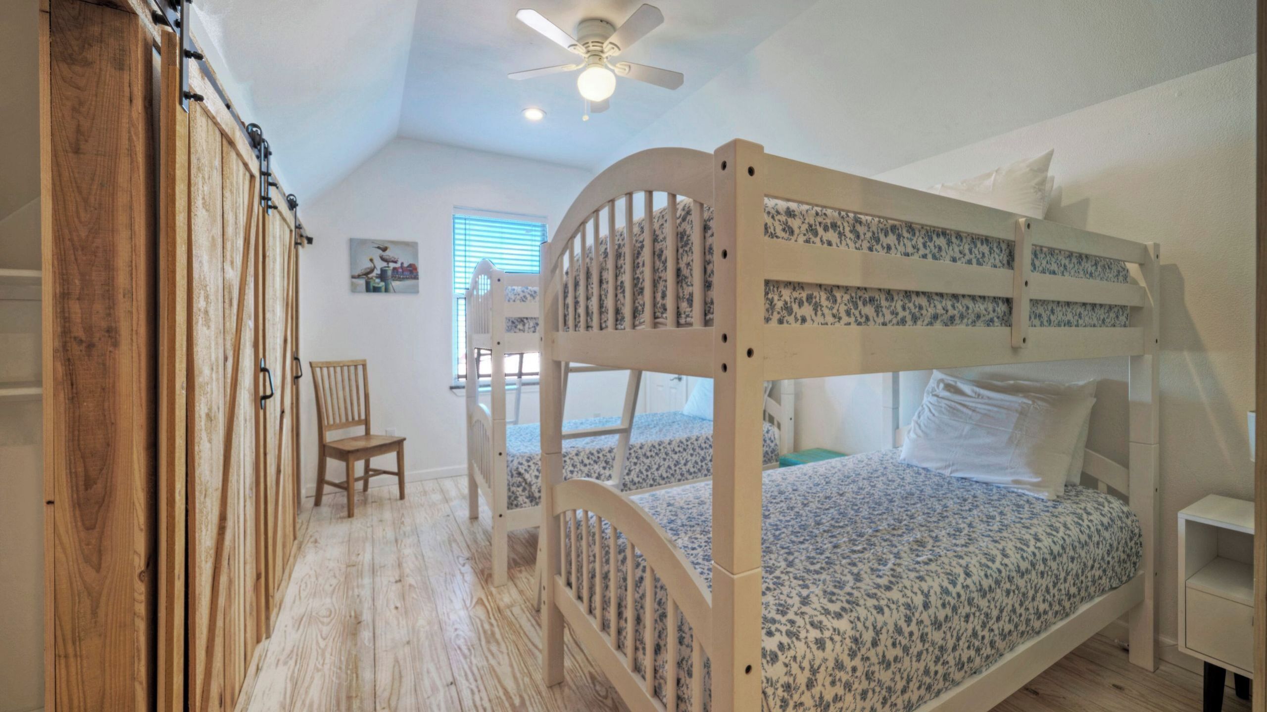 A bunk bed room with a ceiling fan, a chair, and a small table.