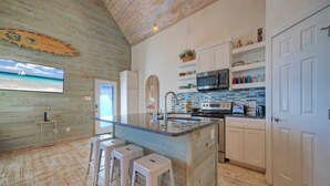 Una cocina con piso de madera, armarios blancos, una isla grande con taburetes, un microondas y un salpicadero de azulejos.