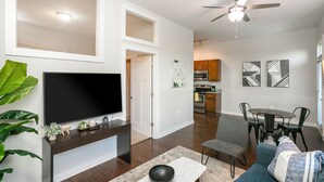 A modern living room with a flat-screen TV, a ceiling fan, and a dining area with a table and chairs. - Music Row w Free Parking  Close to University (Nashville)