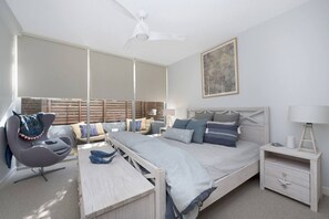 Une chambre à coucher comprenant un lit, des tables de chevet, une chaise, un bureau et un ventilateur de plafond.