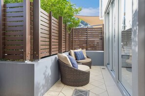 Un balcon agrémenté de meubles en osier, d’une clôture en bois et offrant une vue sur la verdure.