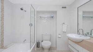 Et moderne badeværelse med en glasafskærmet brusekabine, toilet og vask med spejl.