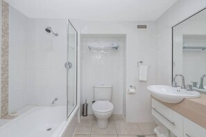 Een moderne badkamer met een douche met glazen wand, een toilet en een wastafel met spiegel.
