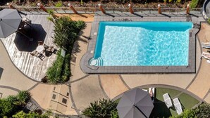 A rectangular swimming pool with a tiled deck surrounding it, equipped with lounge chairs and umbrellas.