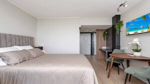 A modern hotel room with a large bed, a desk, and a dining area.