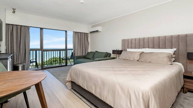 A modern hotel room with a large bed, a desk, and a balcony with a view.