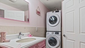 A bathroom with a pink vanity, a sink, a mirror, and a stacked washer and dryer. - GIRLS SUITE w/ BALL PIT! 3 THEMED BEDROOMS & 2 BATH located in CHINATOWN  (Philadelphia)